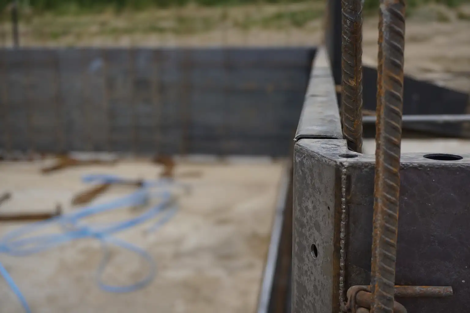 Gros plan sur l’angle d’un bassin en construction : quelques armatures verticales devant une banche de coffrage