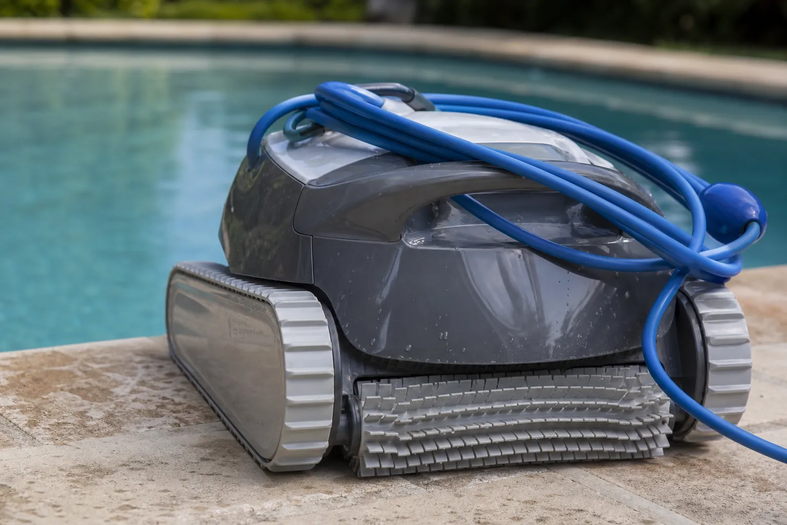 Robot nettoyeur de piscine électrique posé sur la margelle, câble flottant enroulé et brosses visibles